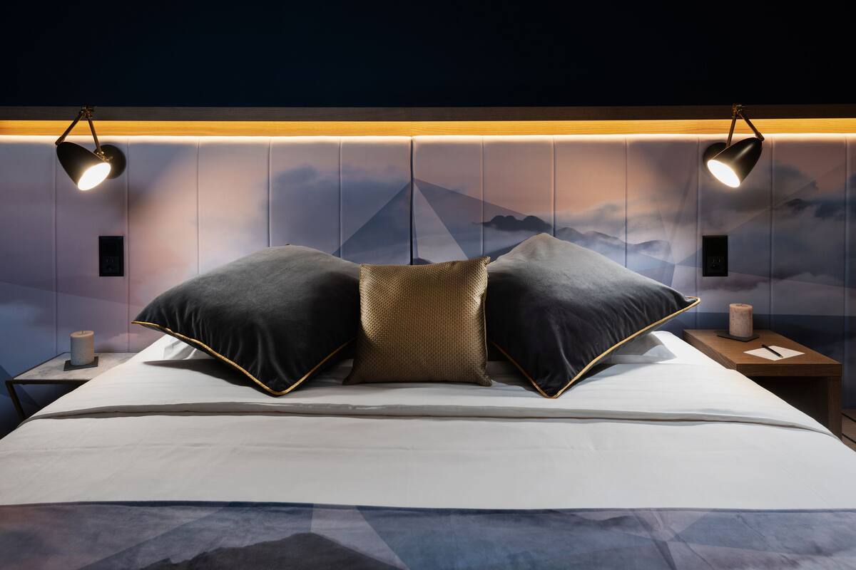 A modern bedroom with a bed, two nightstands, and a wall-mounted lamp.