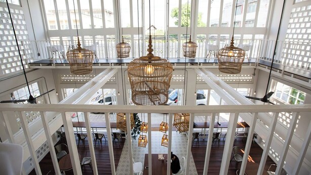 Un área de comedor de varios niveles con candelabros de mimbre, barandillas blancas y ventanas grandes.