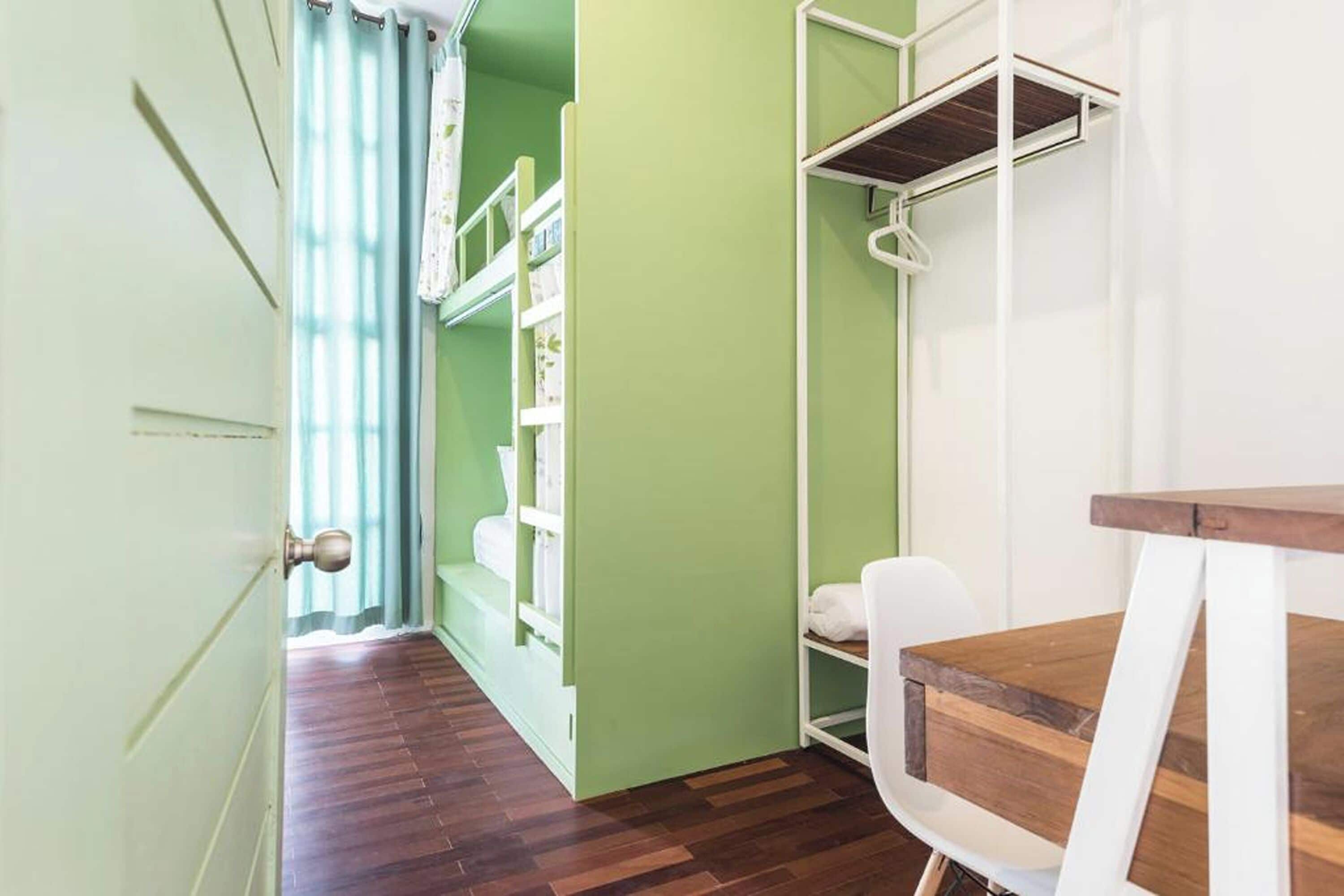 A room with a wooden floor, a white chair, a wooden table, and a green wall with a white shelf unit.