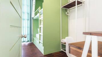 A room with a wooden floor, a white chair, a wooden table, and a green wall with a white shelf unit.
