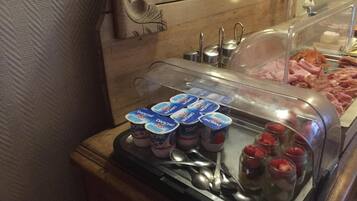 A breakfast buffet with yogurt containers, strawberries, and various meats.