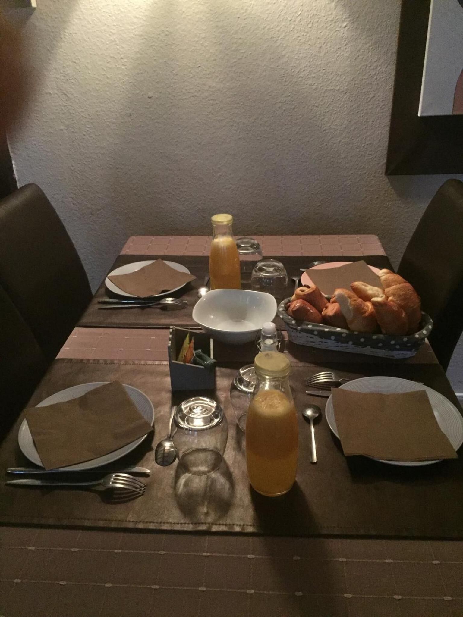 A dining table set with plates, cutlery, napkins, and a basket of bread.