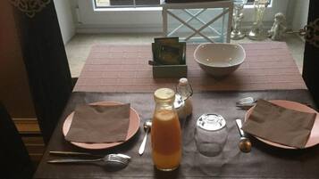 A breakfast table set with plates, cutlery, a glass of orange juice, a basket of croissants, and a candle.