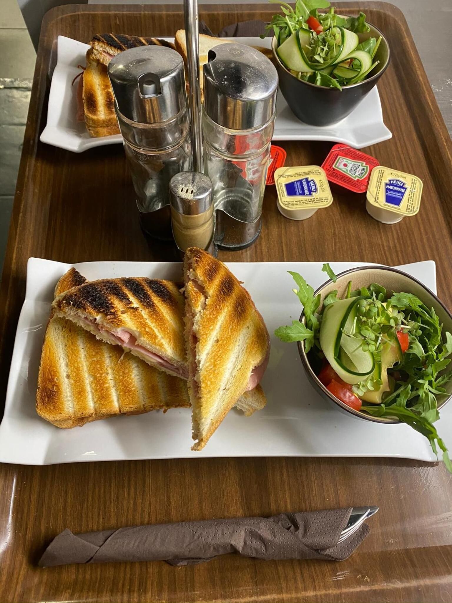 Un sándwich en una bandeja con salsas y una ensalada.