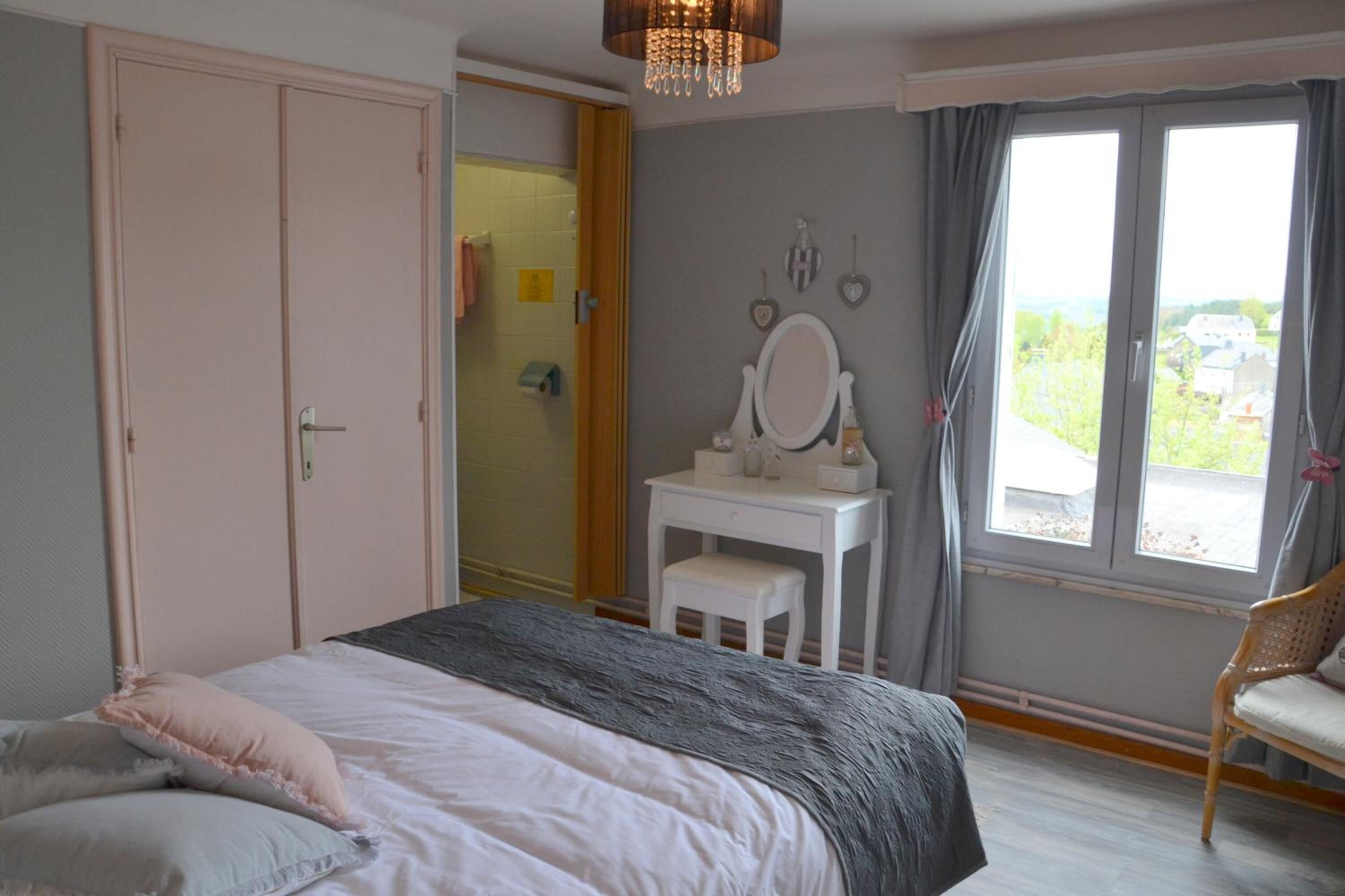 Une chambre à coucher comprenant un lit, une coiffeuse avec un miroir, une chaise et une vue sur l’extérieur par une fenêtre.