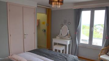 Une chambre à coucher comprenant un lit, une coiffeuse avec un miroir, une chaise et une vue sur l’extérieur par une fenêtre.