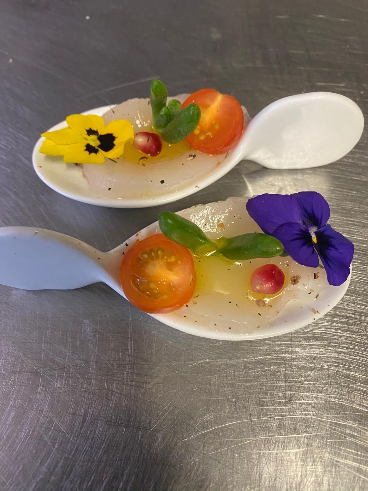 Two white spoons with food on them, placed on a metallic surface.