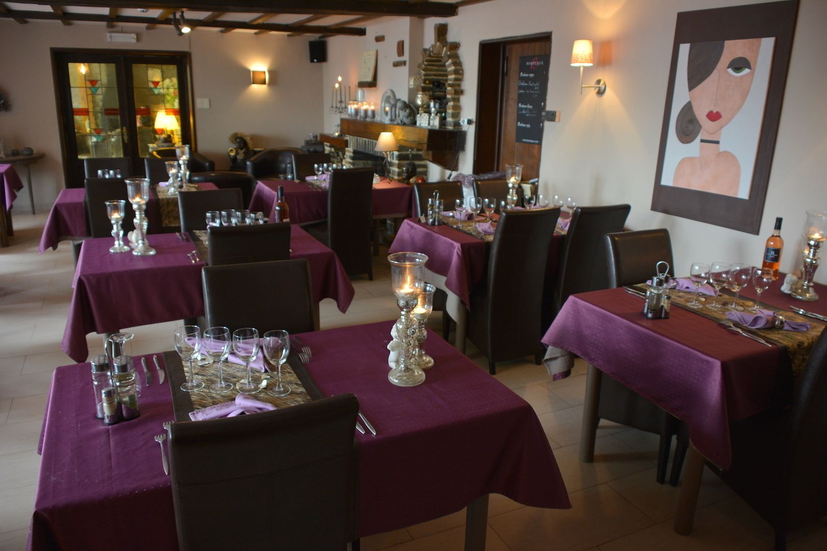 A restaurant with tables set for dining, featuring purple tablecloths and candle centerpieces.