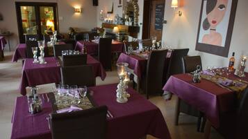 A restaurant with tables set for dining, featuring purple tablecloths and candle centerpieces.