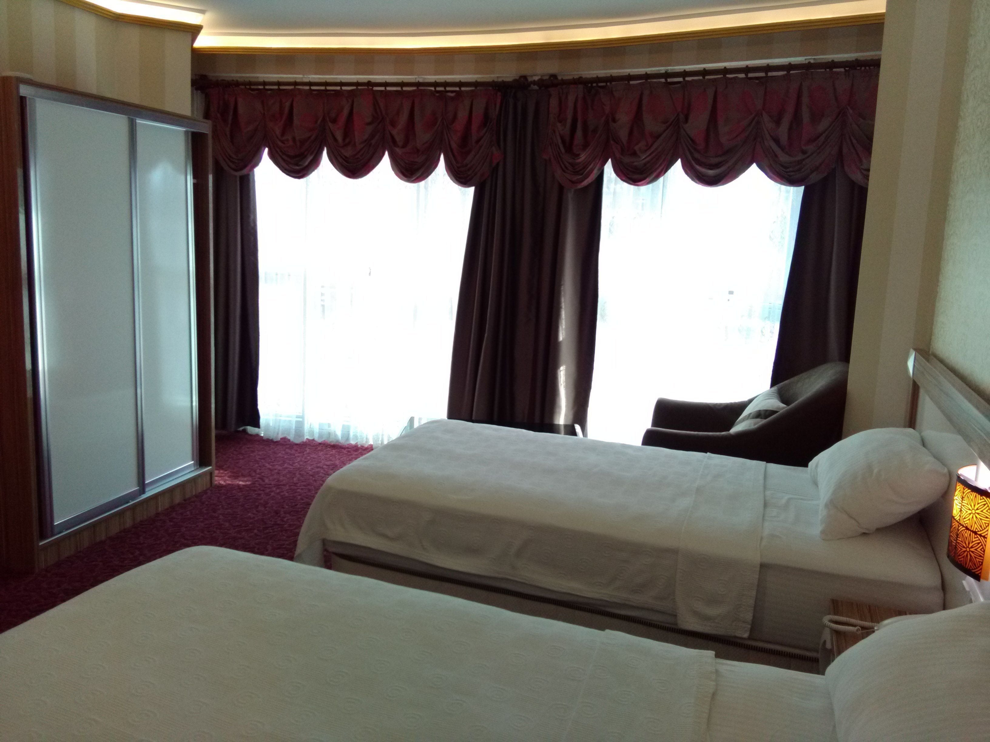 A hotel room with two beds, a wardrobe, and a large window with curtains.