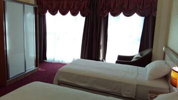 A hotel room with two beds, a wardrobe, and a large window with curtains.