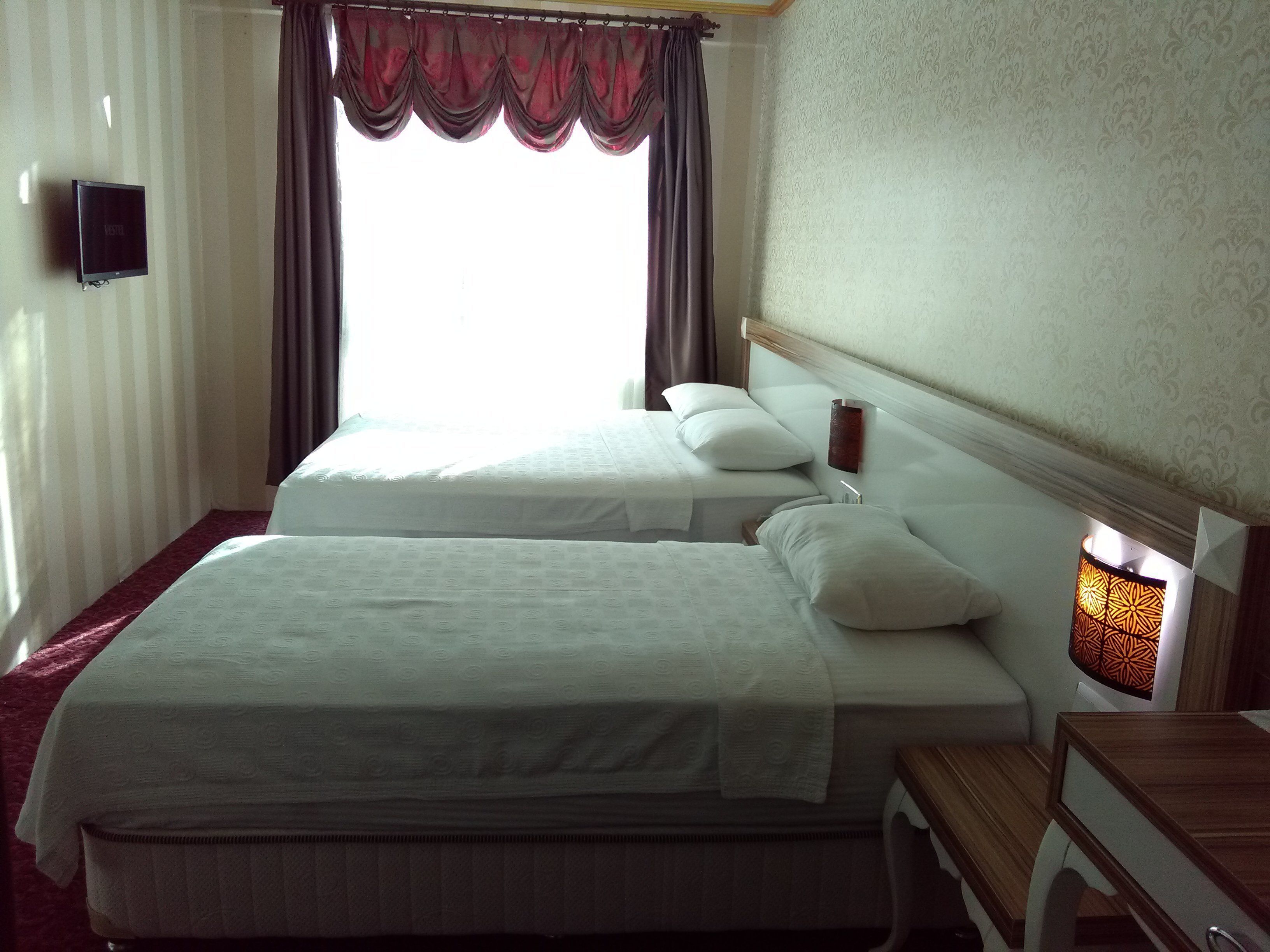 Habitación de hotel con dos camas, una mesita de noche, una lámpara y un televisor en la pared.