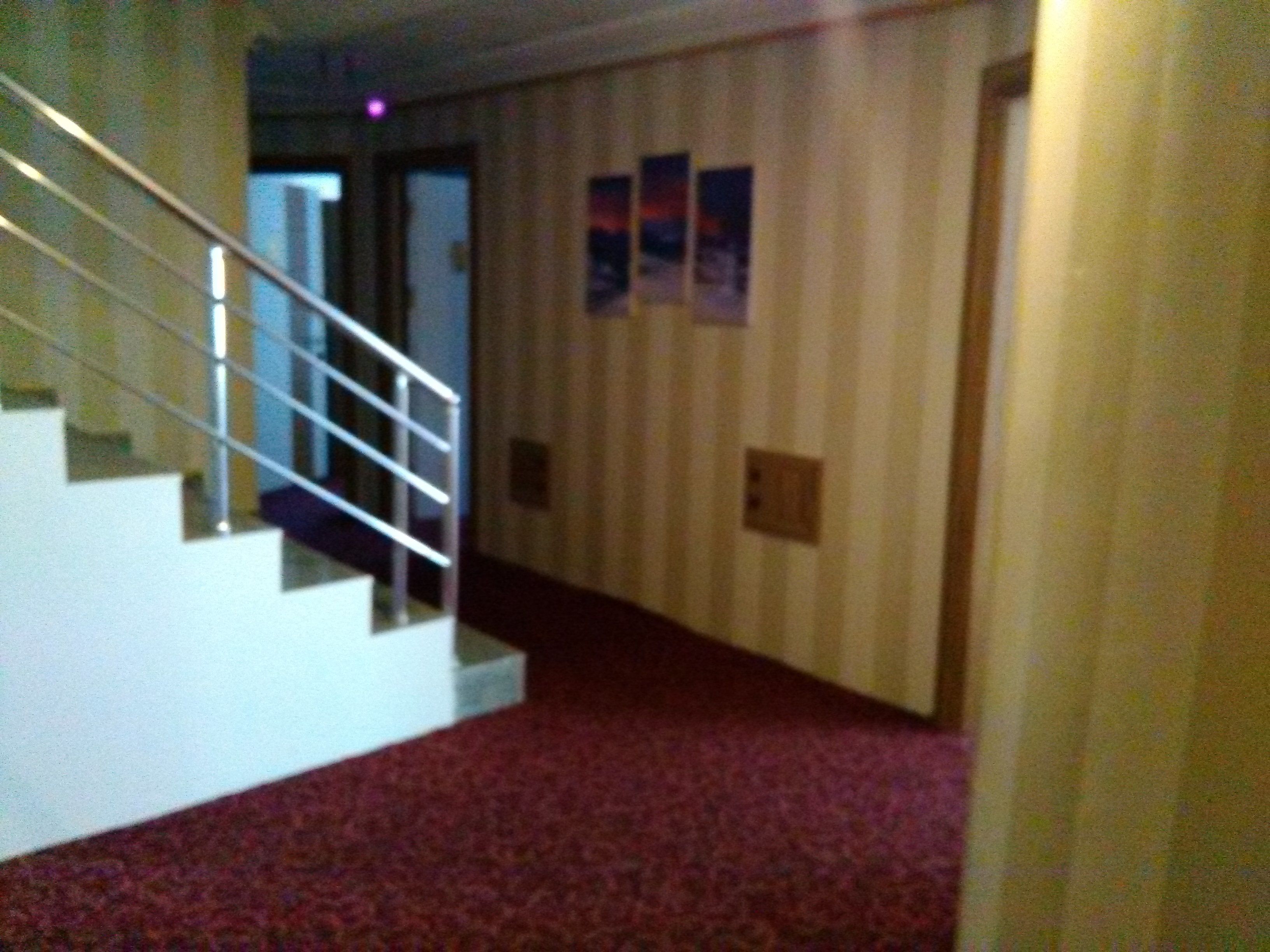 Un pasillo con alfombra roja, una escalera con barandillas blancas y papel tapiz a rayas.