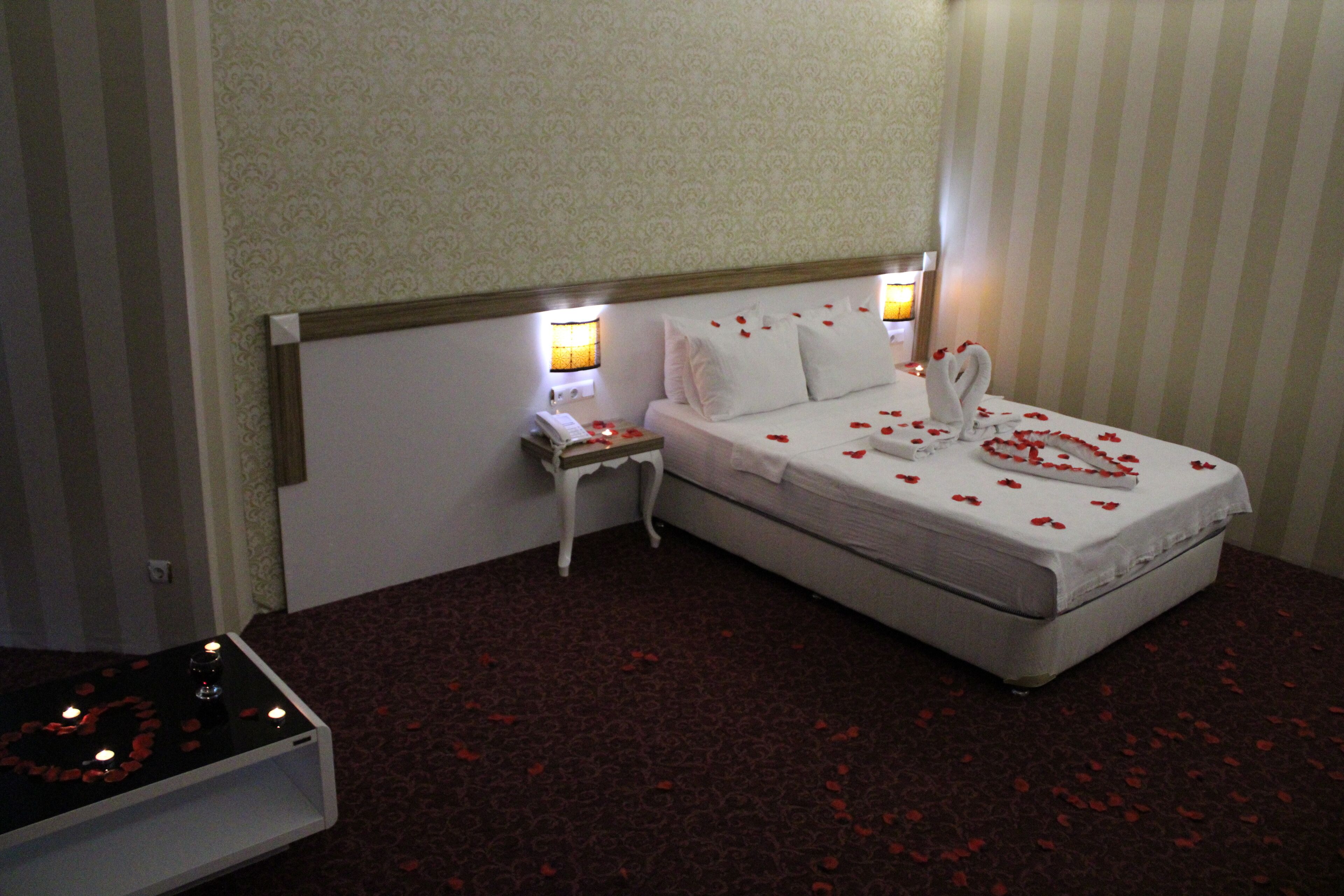 Habitación de hotel ordenada con una cama, lámparas de noche, una mesita de noche y una pequeña mesa con velas.