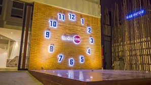 A large illuminated clock with the numbers 1-12 and the words "Service ONE" in the center, mounted on a brick wall. - Service One (Phnom Penh)