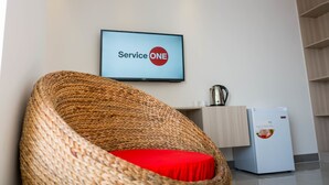 A wicker chair with a red cushion, a television displaying "Service ONE", a small refrigerator, and a wooden cabinet. - Service One (Phnom Penh)