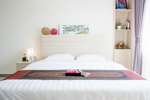 Ein ordentlich bezogenes Bett mit einer dekorativen Tagesdecke, ein Nachttisch mit Lampe und Bilderrahmen sowie ein an der Wand hängendes Kunstwerk über dem Bett.