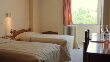 A hotel room with two beds, a nightstand, a vase with flowers, a radiator, and a window with curtains.