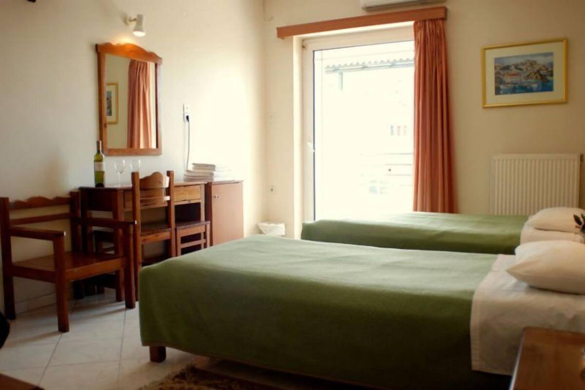 Une chambre d’hôtel avec deux lits simples, un bureau en bois avec une chaise, un miroir et une fenêtre avec des rideaux.