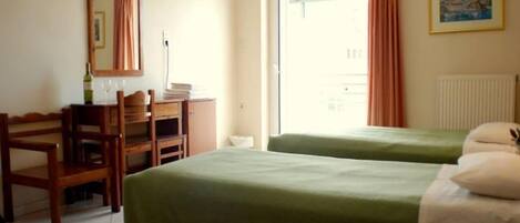 A hotel room with two single beds, a wooden desk with a chair, a mirror, and a window with curtains.