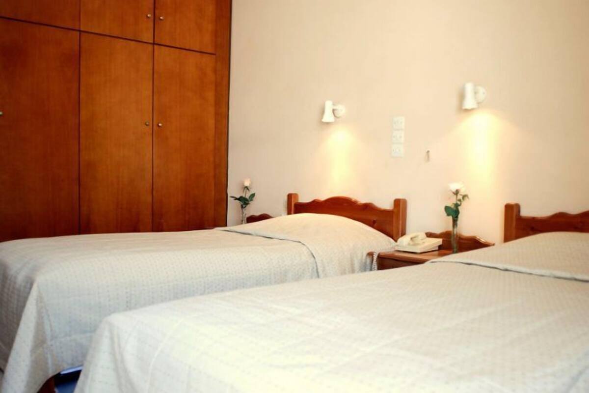 Une chambre d’hôtel avec deux lits simples, des têtes de lit en bois, des tables de chevet avec des lampes et une grande armoire.