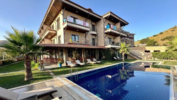 Un edificio de dos pisos con piscina, zona de estar exterior y vista a un paisaje montañoso.
