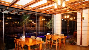 Un restaurante con mesas y sillas de madera, ventanas amplias y lámparas colgantes.