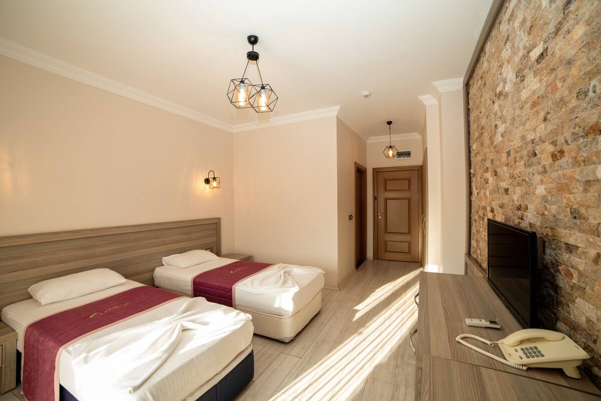 Habitación de hotel con dos camas, un televisor de pantalla plana, un teléfono y una pared de ladrillo.