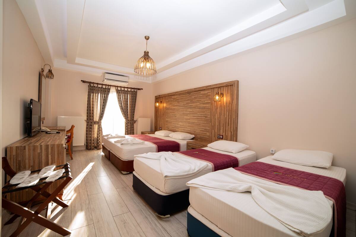 Una habitación de hotel con tres camas, un escritorio con una silla y un televisor.