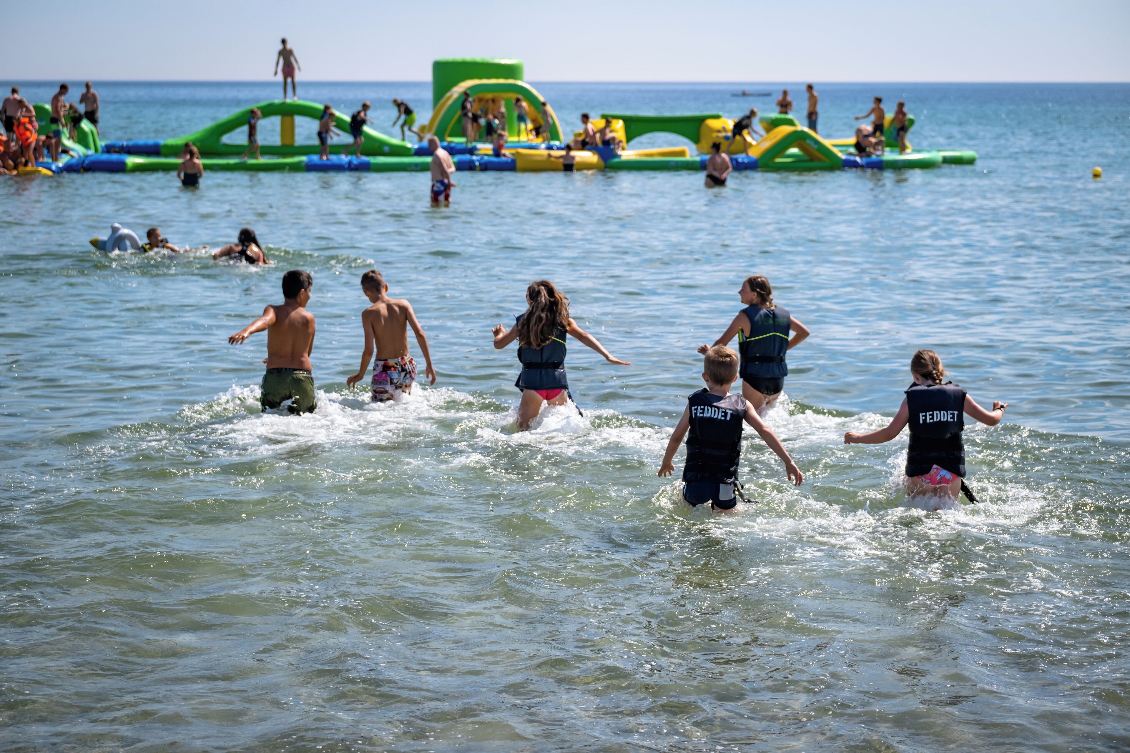 Una playa con estructuras acuáticas inflables y gente nadando y jugando en el agua.