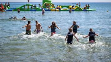 Una playa con estructuras acuáticas inflables y gente nadando y jugando en el agua.
