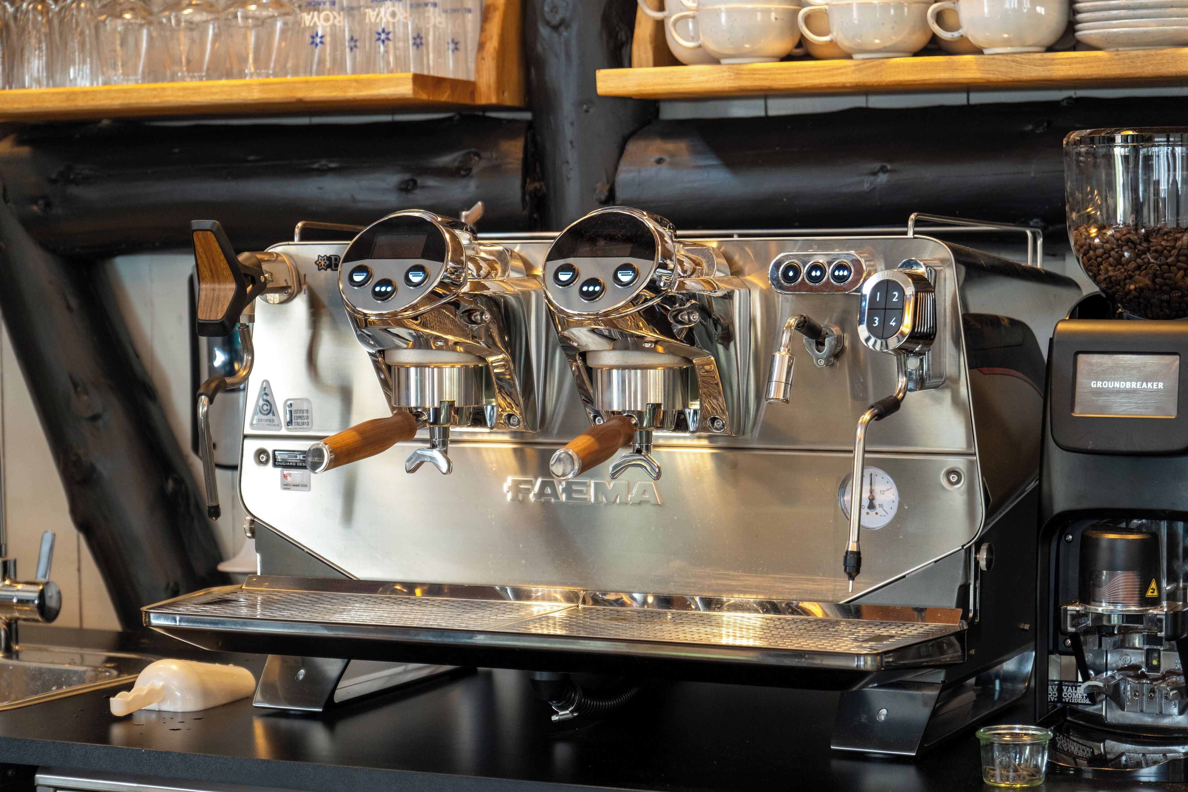 A professional espresso machine with a digital display and wooden handles, placed on a commercial kitchen counter.