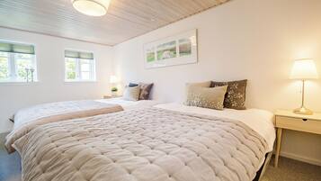 Una cama doble con cubrecama acolchado color beige, dos mesitas de noche con lámparas y un cuadro de paisaje enmarcado en la pared.