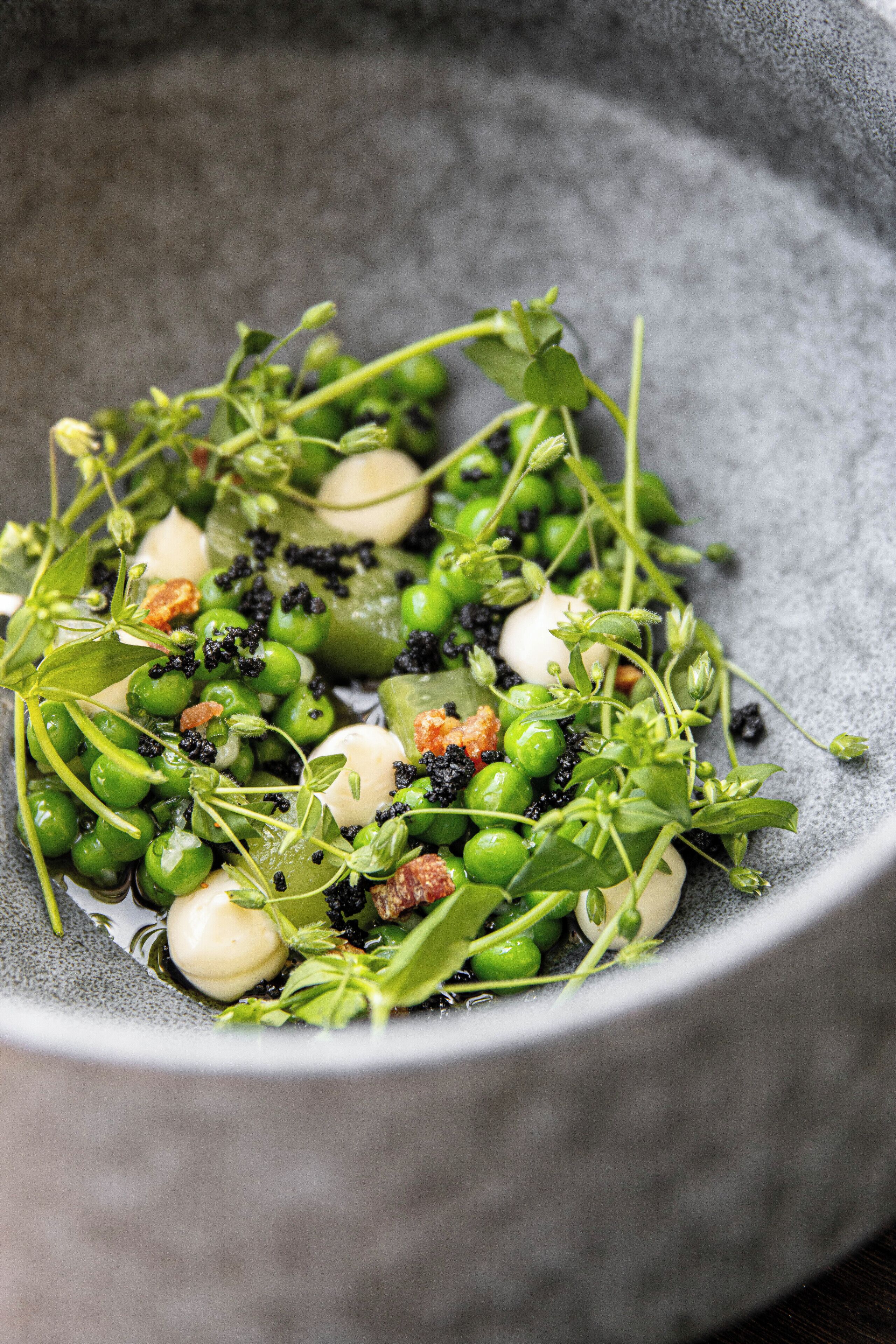 En skål med grøn ærtesalat, blandede grøntsager og nødder.