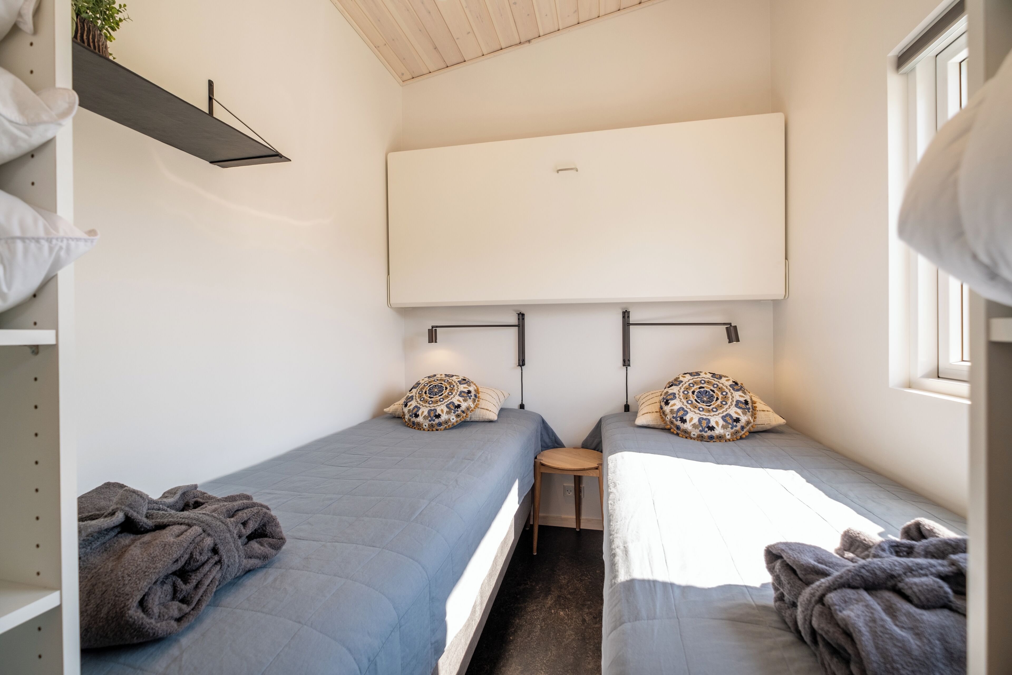 A compact room with two single beds, a small table, and a wall-mounted air conditioner.