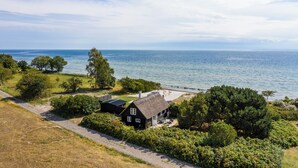 A coastal house with a thatched roof, surrounded by dense greenery and a view of the sea. - Feddet Strand Resort (Faxe)