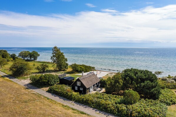 Una casa costera con techo de paja, rodeada de vegetación exuberante y vistas al mar.
