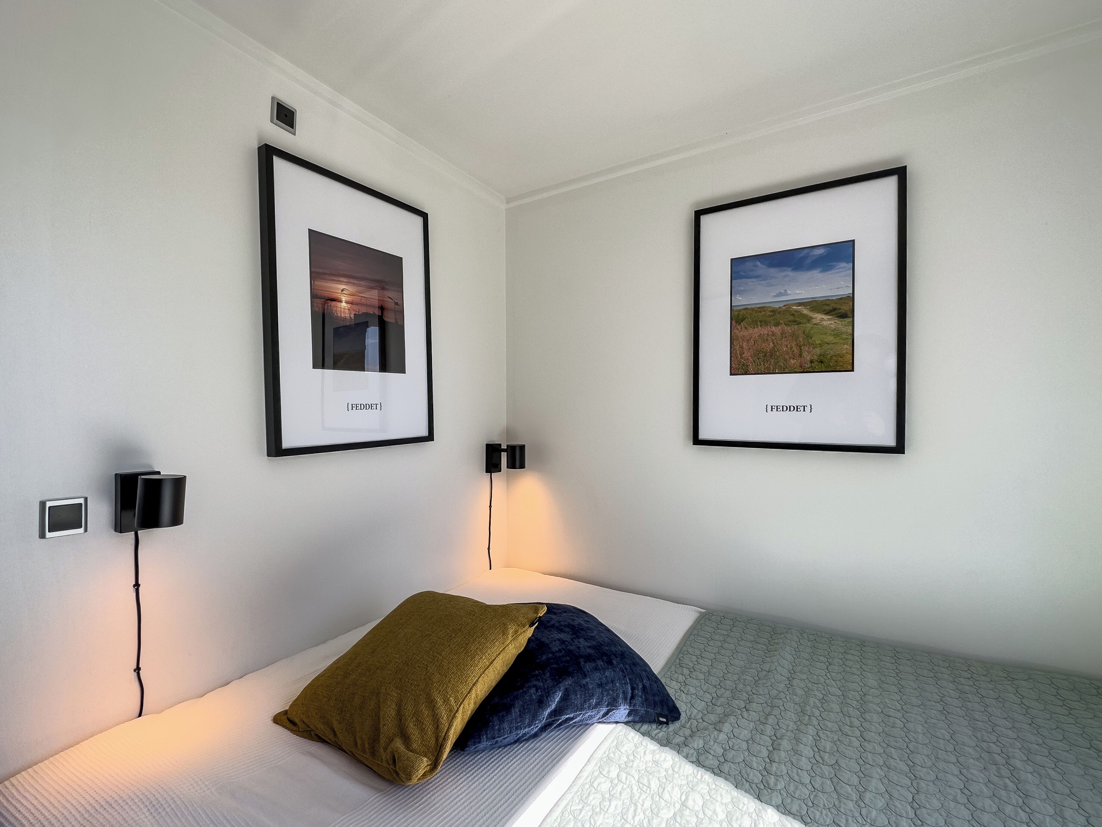 A room with a bed, two framed pictures on the wall, a wall-mounted lamp, and a small picture frame.