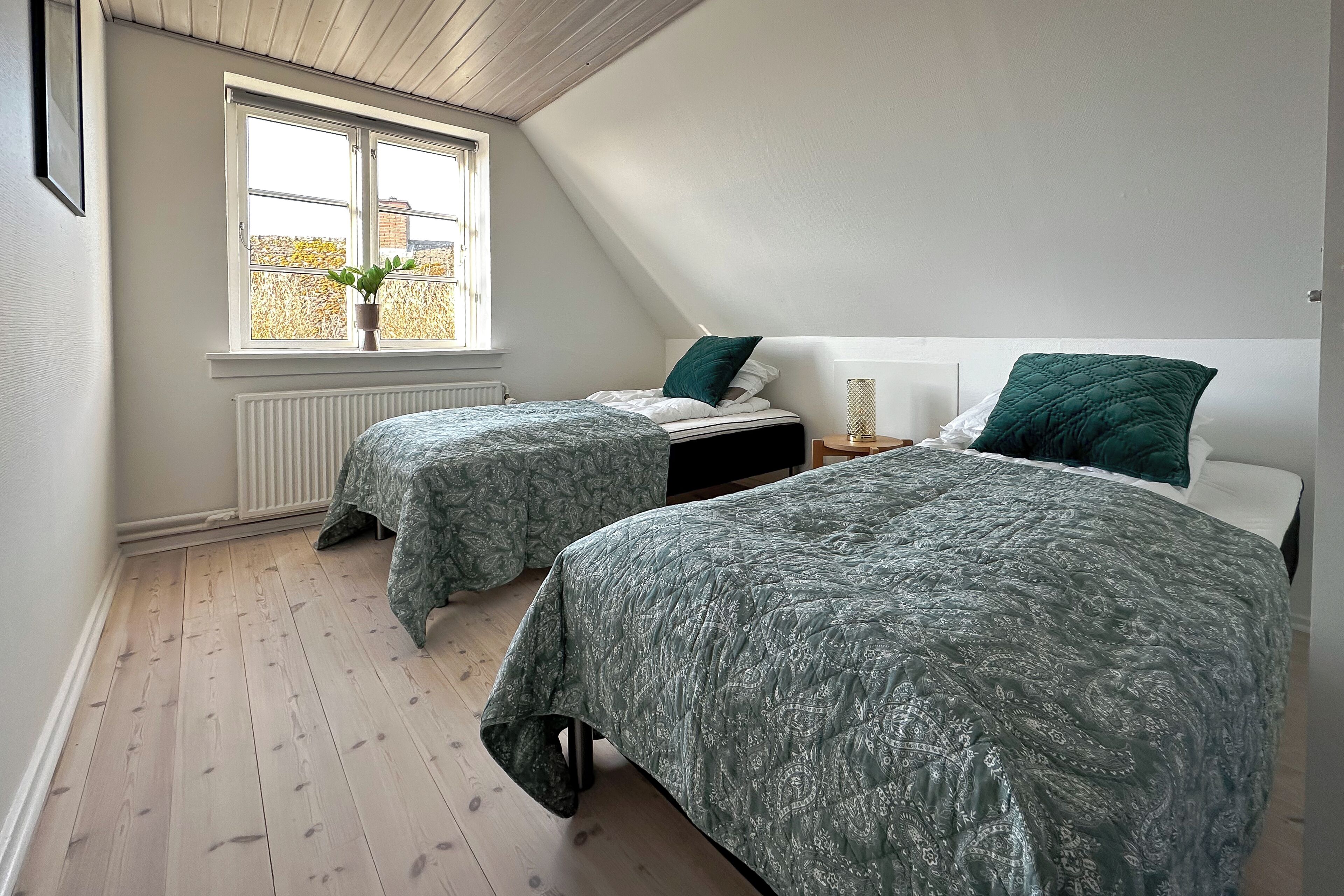 Een slaapkamer met twee bedden, een raam met uitzicht en een radiator.