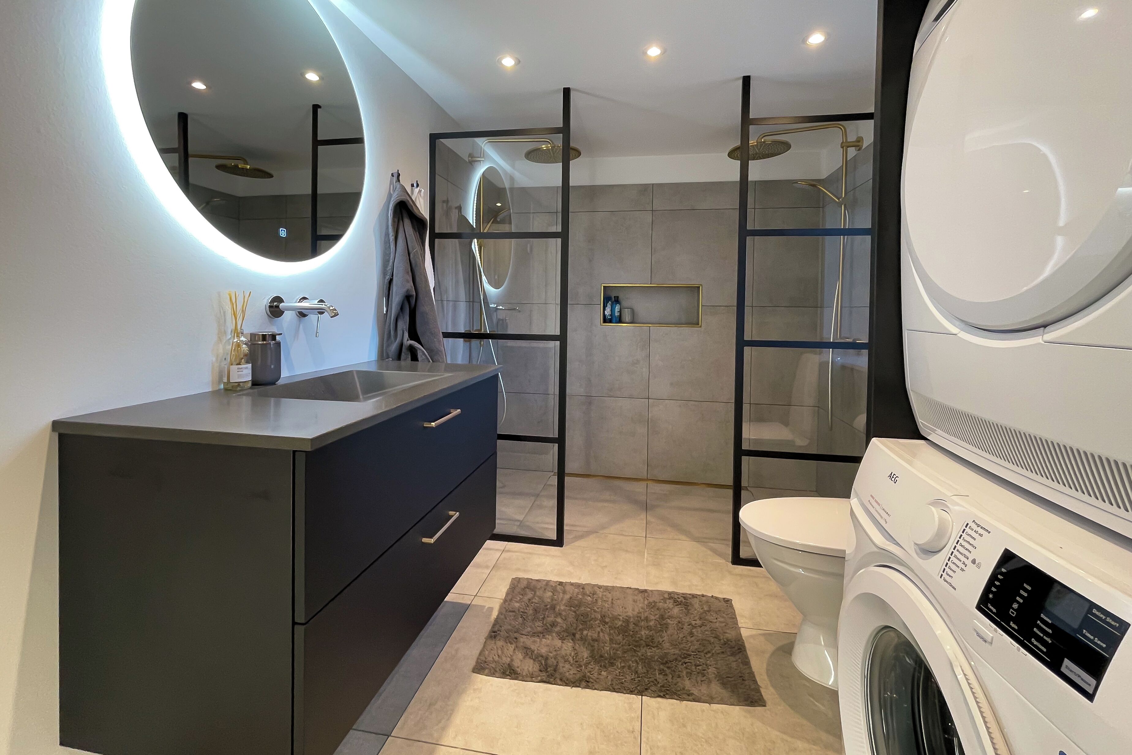 A modern bathroom with a vanity, a toilet, a shower, and a washing machine.