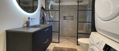 A modern bathroom with a vanity, a toilet, a shower, and a washing machine.