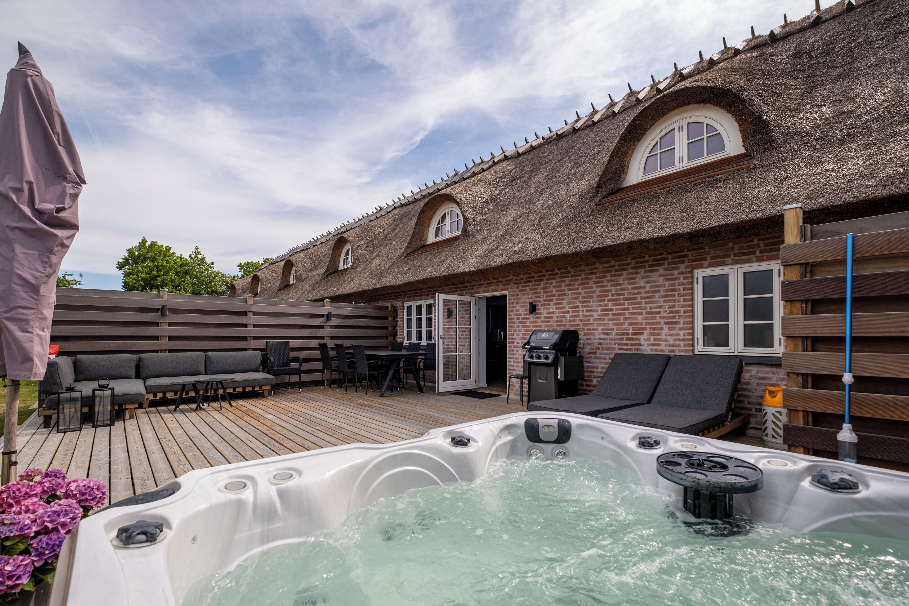 Un jacuzzi en una terraza de madera con un edificio de ladrillo al fondo.