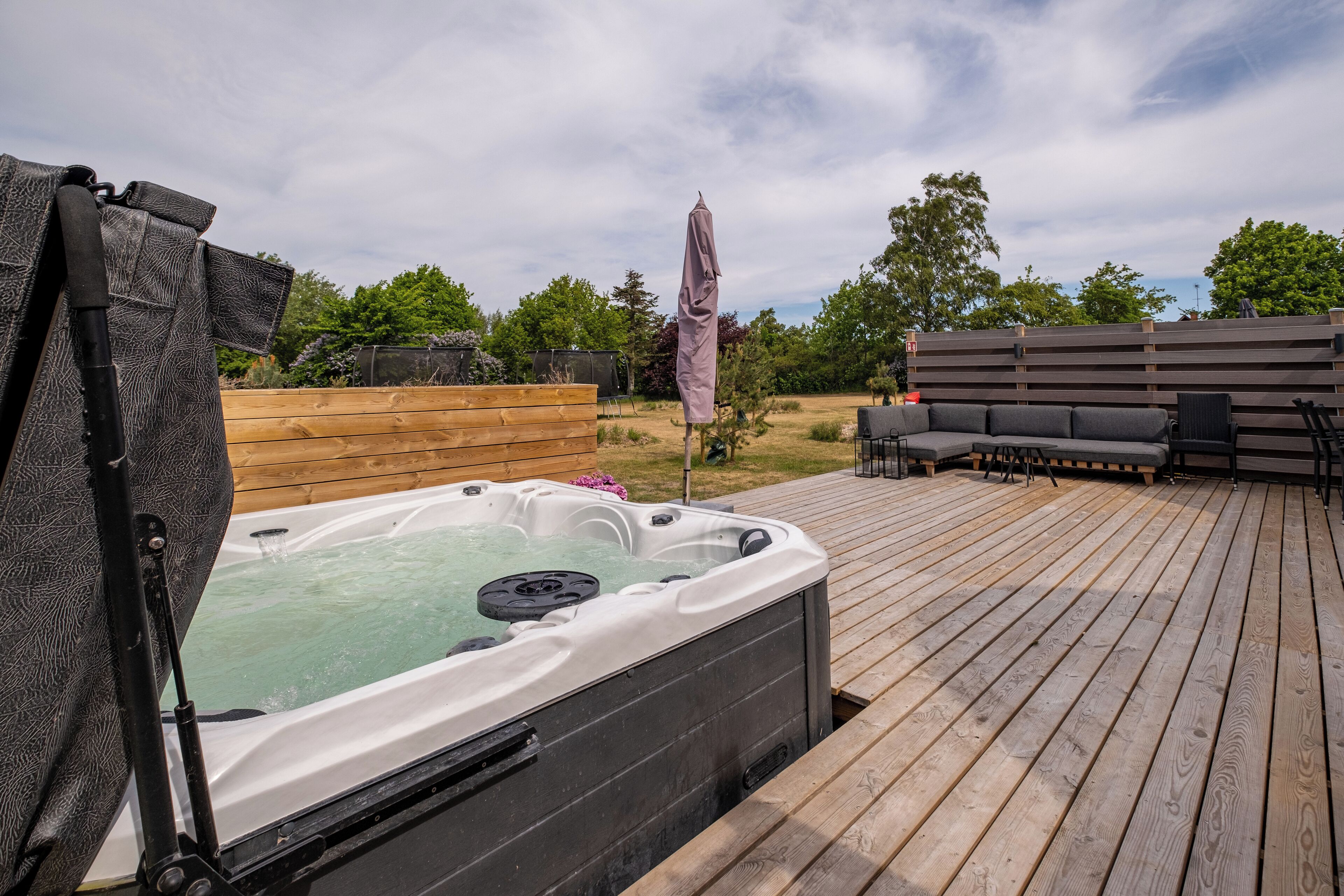 Un bain à remous sur une terrasse en bois, agrémentée d’un parasol, d’une clôture en bois et de mobilier d’extérieur.