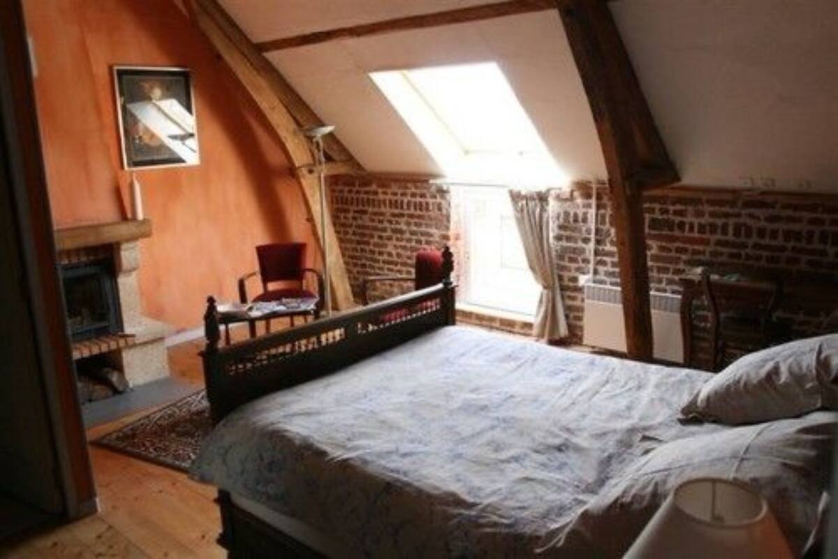 A cozy bedroom with a bed, a chair, a fireplace, and a skylight.