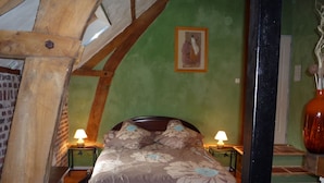 Een slaapkamer met een houten plafond, een bed met bloemenbedrukking, twee nachtkastjes met lampen, en een groene muur met een ingelijst schilderij.