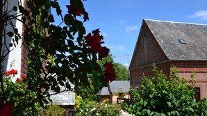 Een landelijk gebouw met een schuin dak, omgeven door weelderig groen en bloeiende planten.