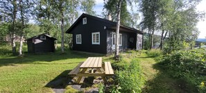 A rustic cabin with a wooden deck and a small shed in a wooded area.