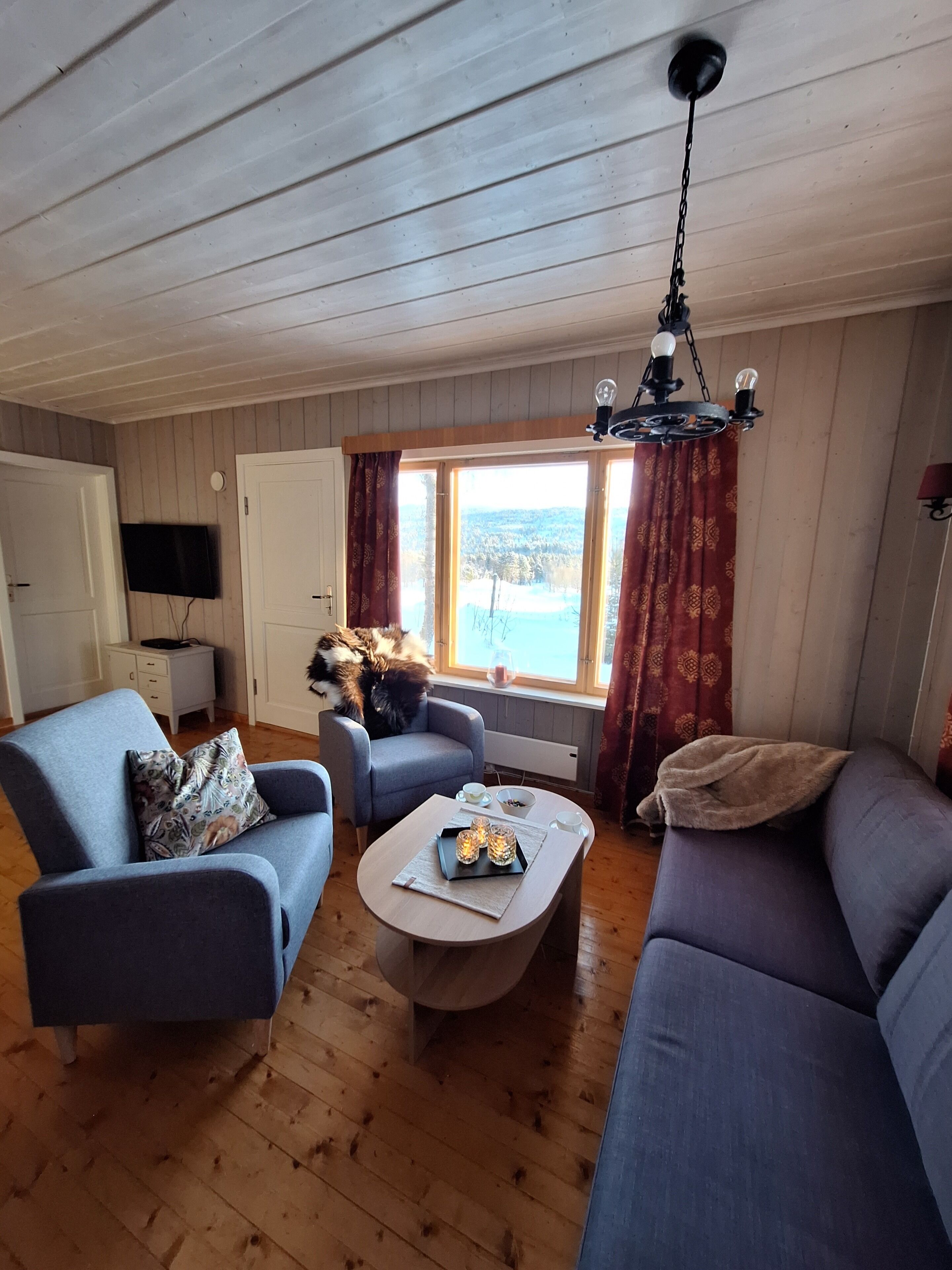 A cozy living room with wooden floors, a sofa, a chair, a coffee table, and a TV mounted on the wall.