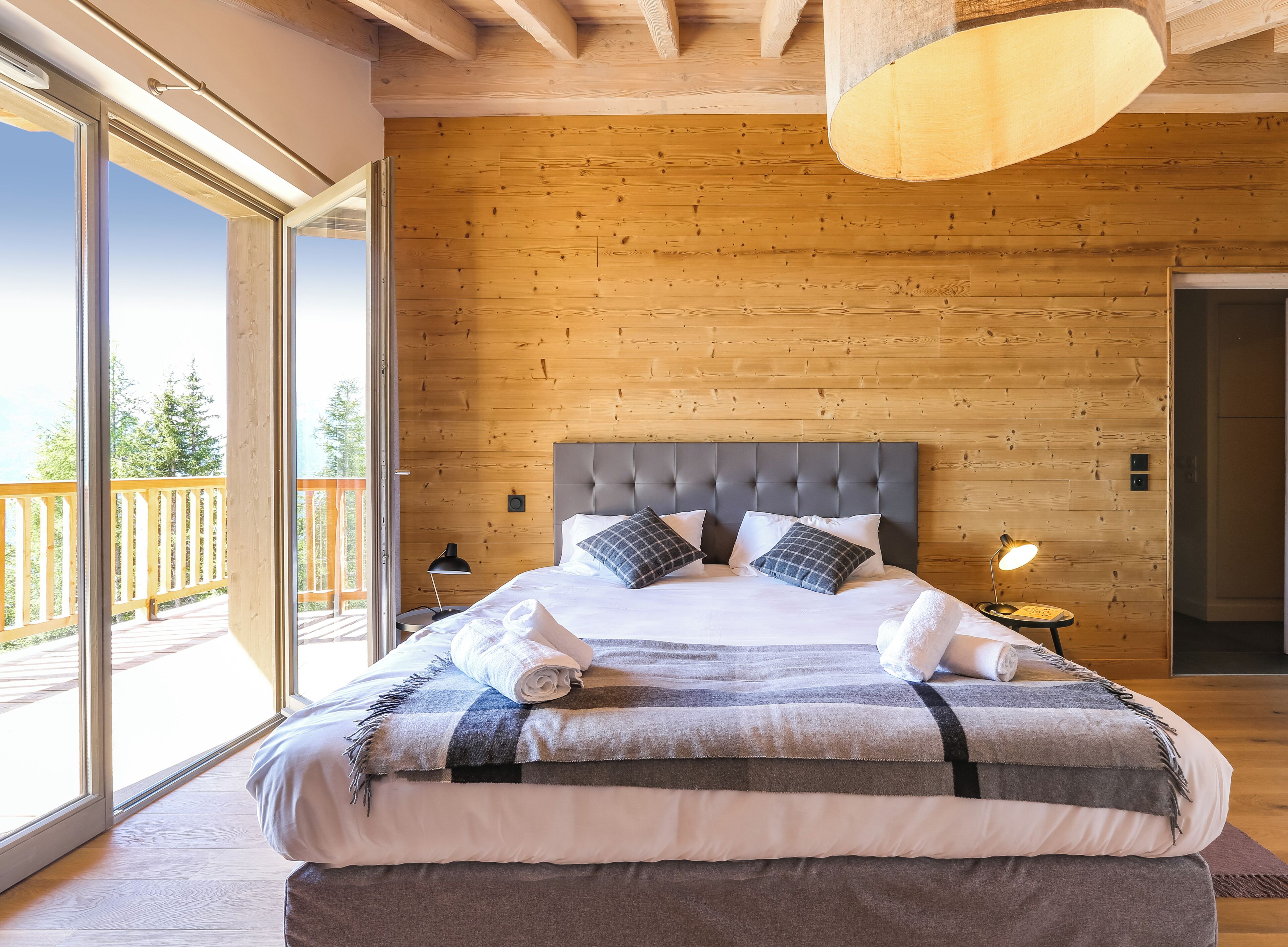 Une chambre avec un grand lit, des murs en bois, un balcon et un luminaire au plafond.