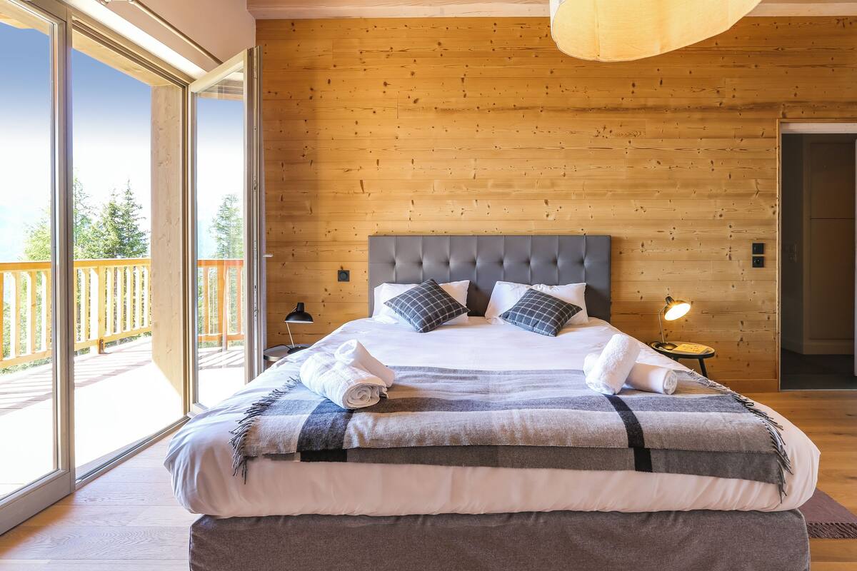 Une chambre avec un grand lit, des murs en bois, un balcon et un luminaire moderne au plafond.